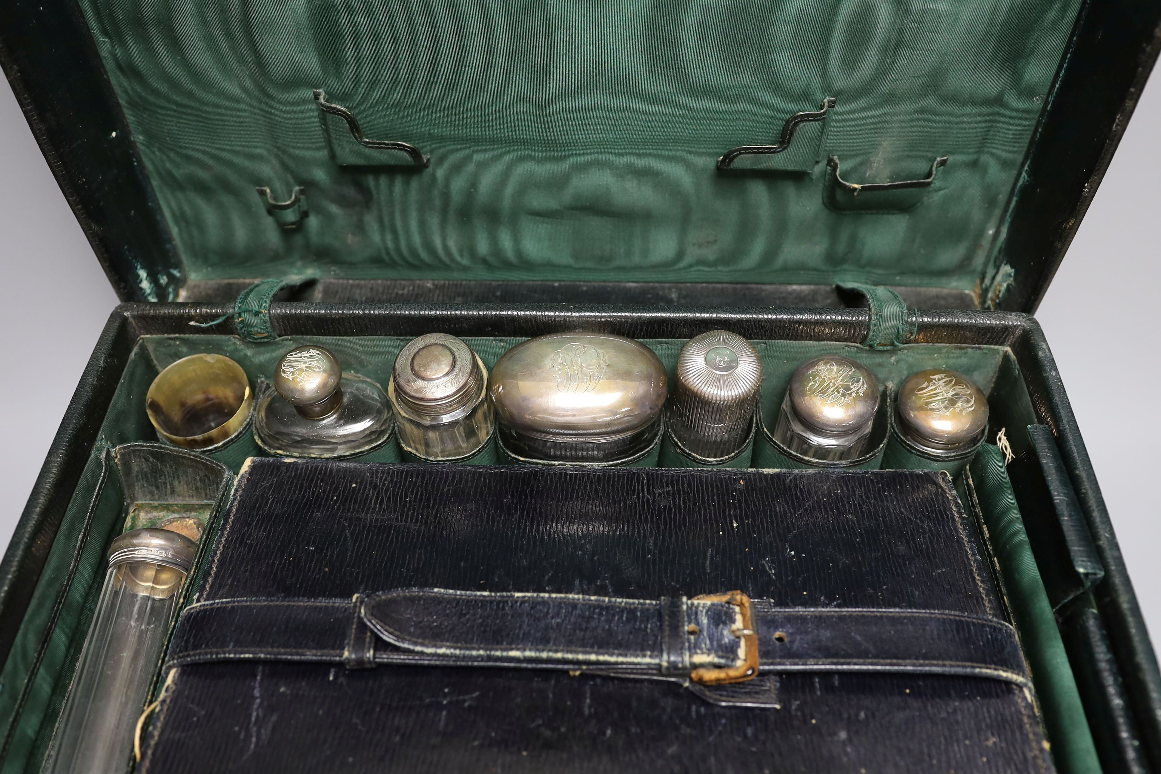 An early 20th century travelling toilet case by Cornhill, London, with seven harlequin silver mounted toilet jars, nail implements and leather stationary case, various dates and makers.